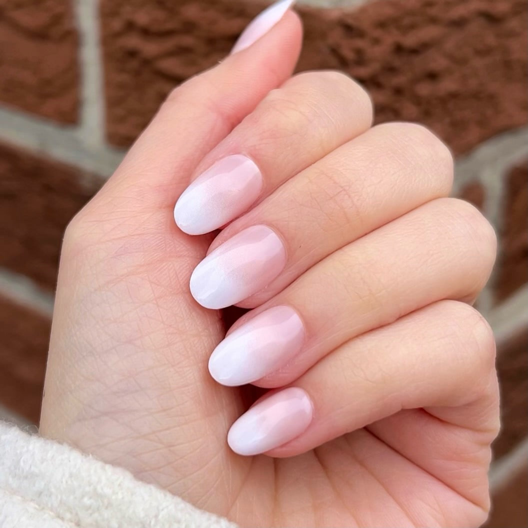 Round Short Pink Ombre Nails on female hand with brick backdrop
