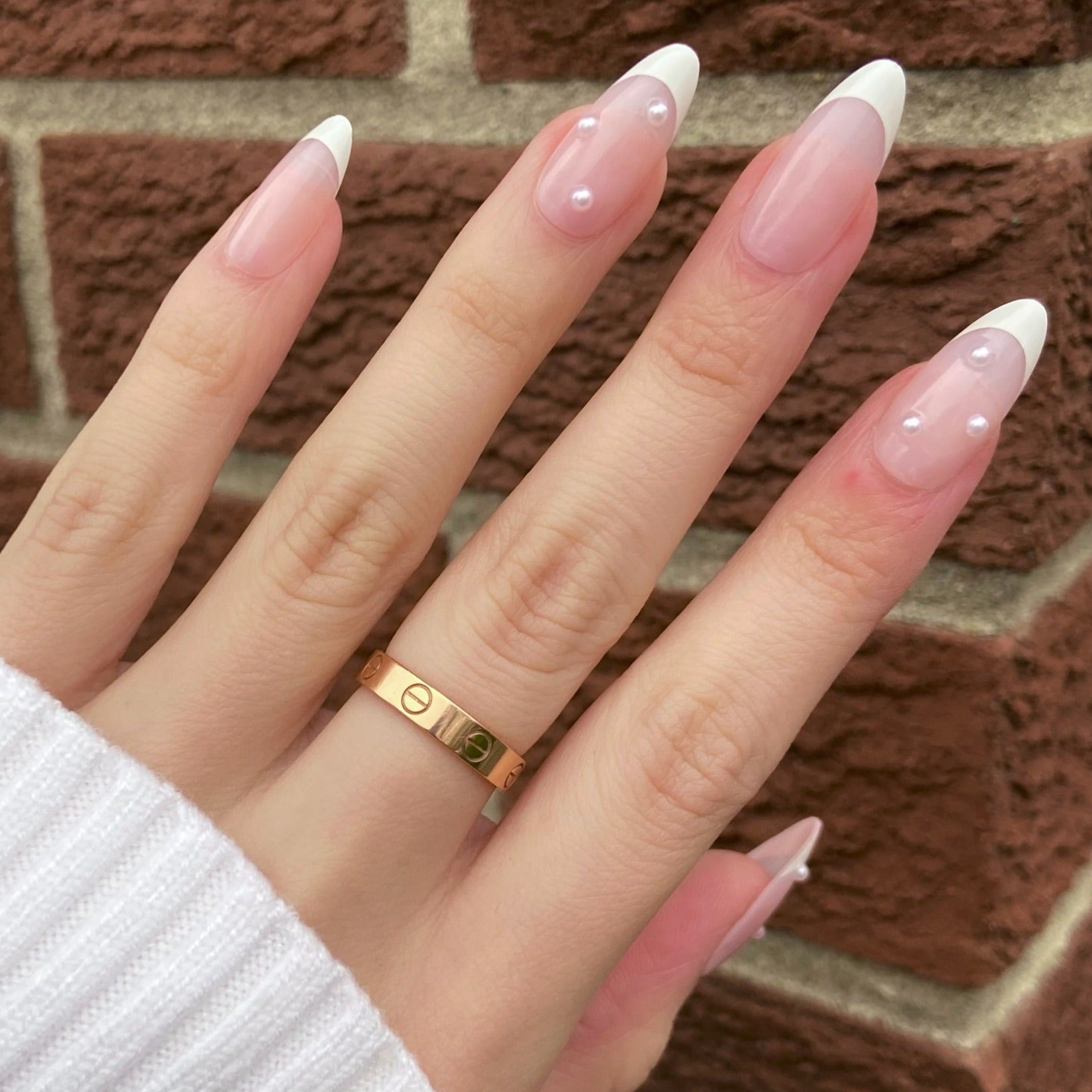 pink french tip nails with pearls on female hand with brick backdrop