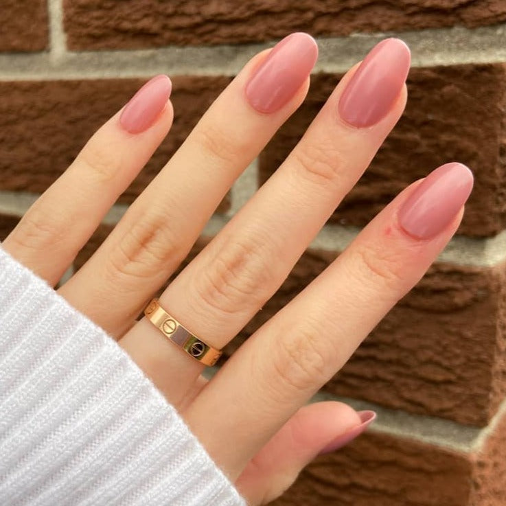rose pink nails on female model hand with brick wall backdrop