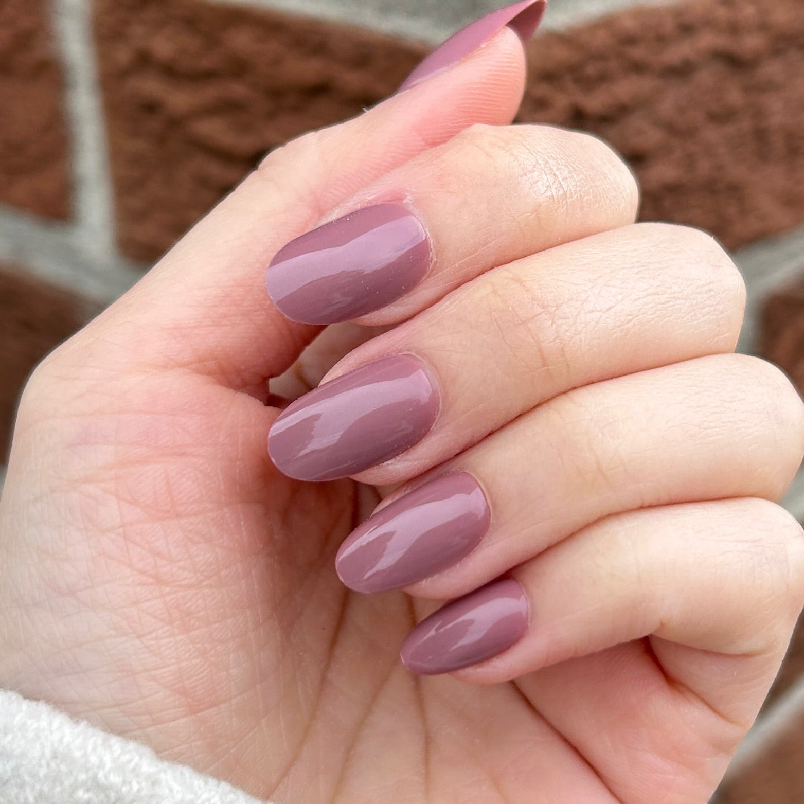 Round short mauve nails on female hand with brick backdrop