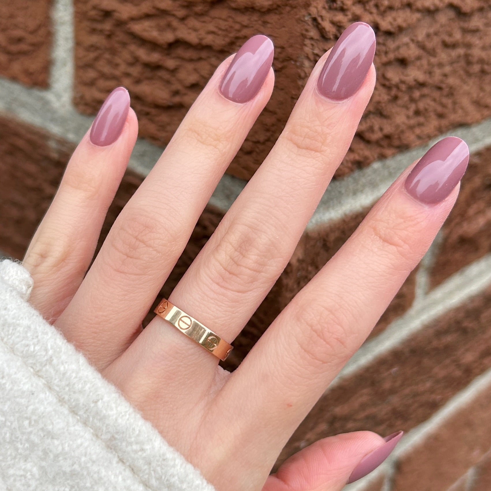 Short round mauve nails on female hand brick backdrop